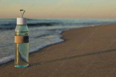 Glass bottle with water on wet sand near sea at sunset. Space for text Photo of Glass bottle with water on wet sand near sea at sunset. Space for text