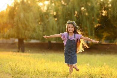 Cute little girl wearing flower wreath outdoors at sunset, space for text. Child spending time in nature Photo of Cute little girl wearing flower wreath outdoors at sunset, space for text. Child spending time in nature