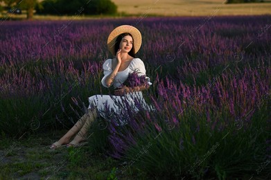 Beautiful young woman with bouquet sitting in lavender field at sunset Photo of Beautiful young woman with bouquet sitting in lavender field at sunset