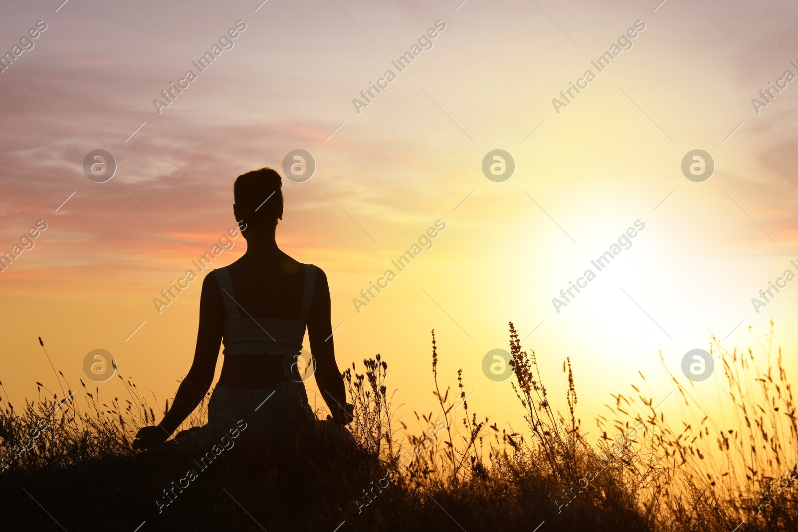 Silhouette of woman meditating outdoors at sunset, back view. Space for text Photo of Silhouette of woman meditating outdoors at sunset, back view. Space for text