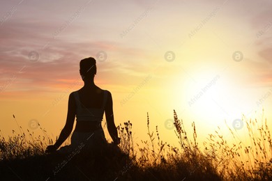 Silhouette of woman meditating outdoors at sunset, back view. Space for text Photo of Silhouette of woman meditating outdoors at sunset, back view. Space for text