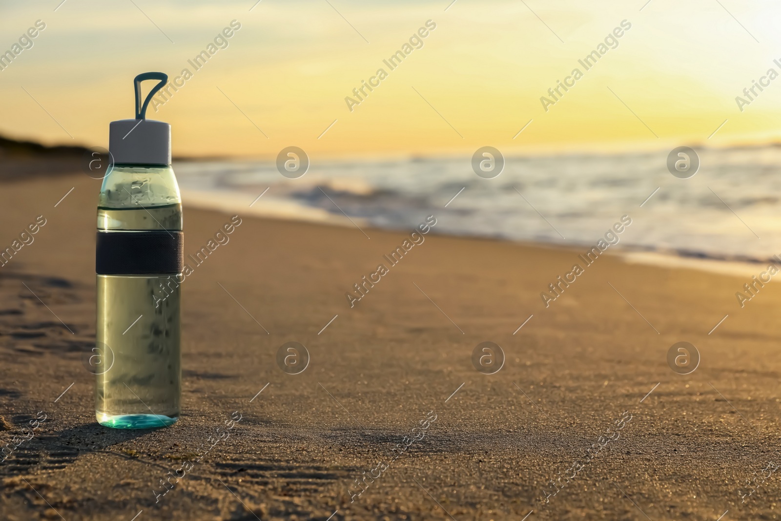Glass bottle with water on wet sand near sea at sunset. Space for text Photo of Glass bottle with water on wet sand near sea at sunset. Space for text