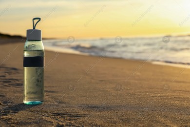 Glass bottle with water on wet sand near sea at sunset. Space for text Photo of Glass bottle with water on wet sand near sea at sunset. Space for text