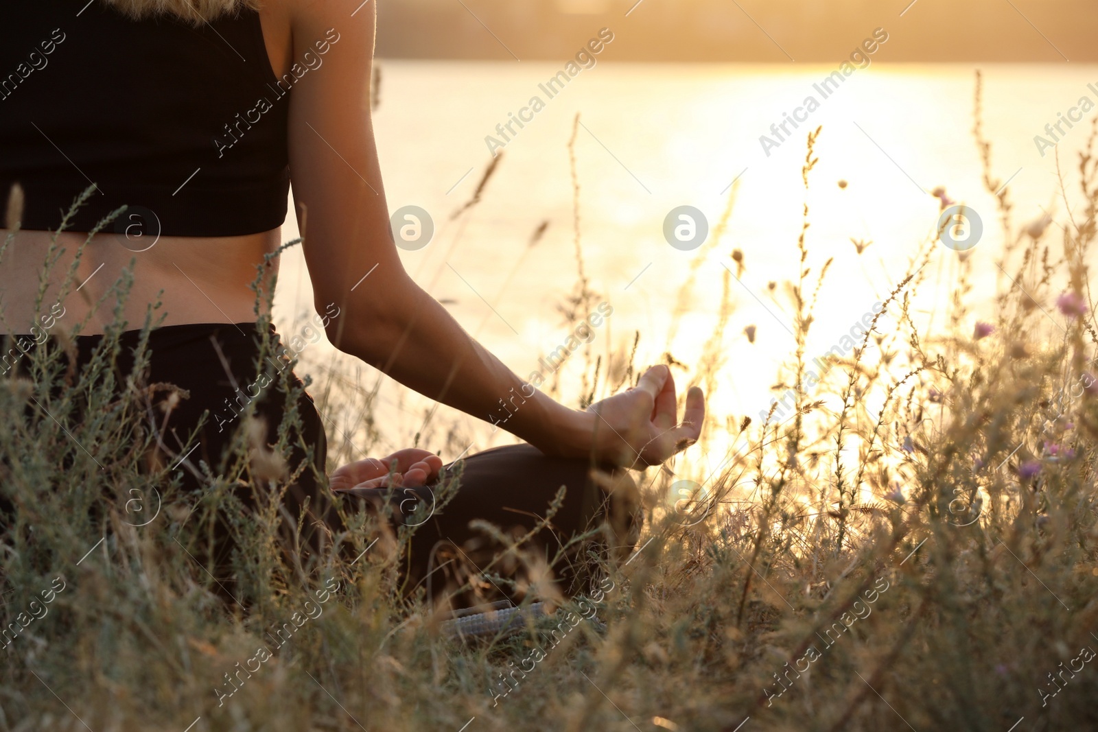 Young woman meditating near river at sunset, closeup Photo of Young woman meditating near river at sunset, closeup