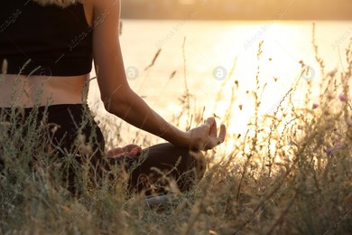 Young woman meditating near river at sunset, closeup Photo of Young woman meditating near river at sunset, closeup