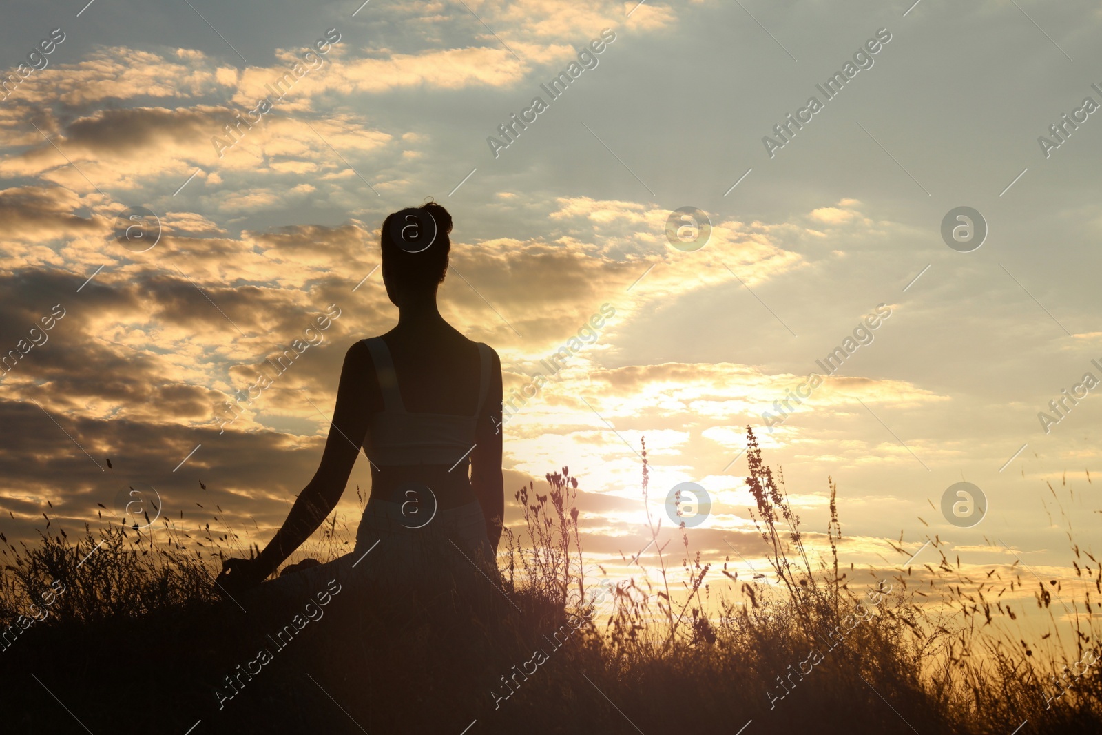 Silhouette of woman meditating outdoors at sunset, back view. Space for text Photo of Silhouette of woman meditating outdoors at sunset, back view. Space for text