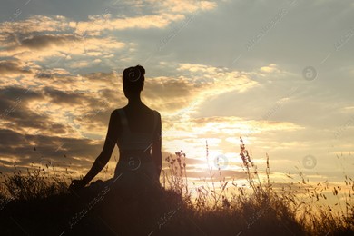 Silhouette of woman meditating outdoors at sunset, back view. Space for text Photo of Silhouette of woman meditating outdoors at sunset, back view. Space for text