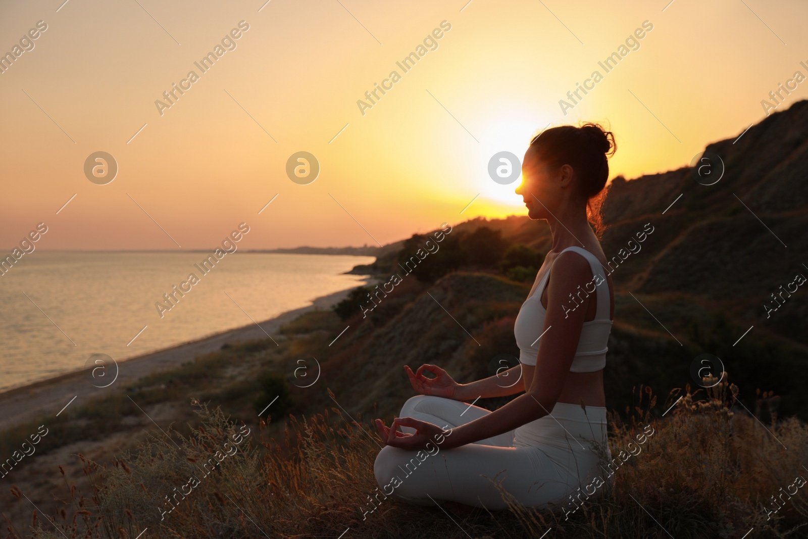 Mature woman meditating on hill near sea at sunset. Space for text Photo of Mature woman meditating on hill near sea at sunset. Space for text
