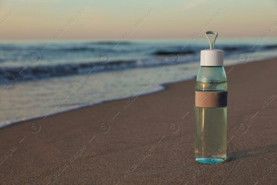 Glass bottle with water on wet sand near sea at sunset. Space for text Photo of Glass bottle with water on wet sand near sea at sunset. Space for text