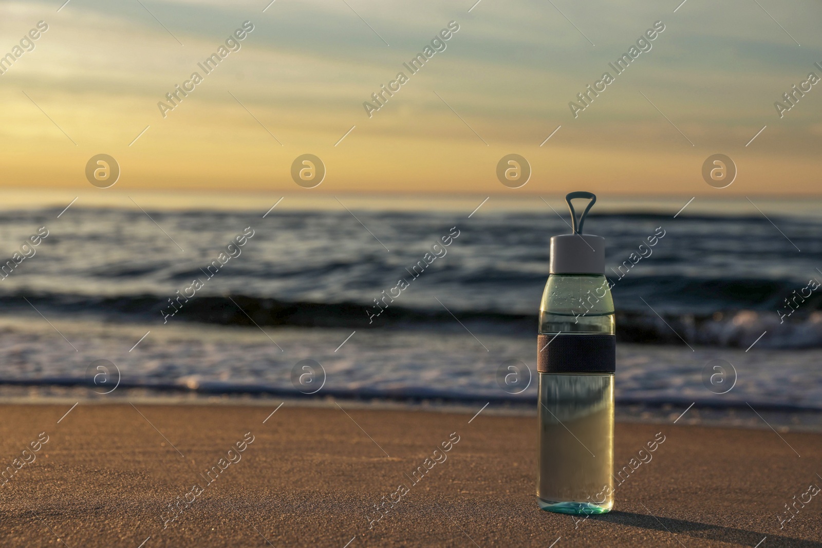 Glass bottle with water on wet sand near sea at sunset. Space for text Photo of Glass bottle with water on wet sand near sea at sunset. Space for text