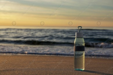 Glass bottle with water on wet sand near sea at sunset. Space for text Photo of Glass bottle with water on wet sand near sea at sunset. Space for text