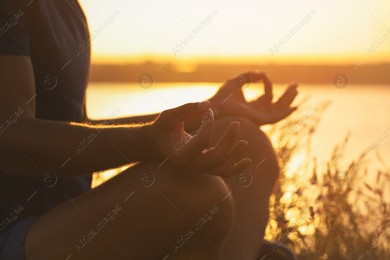 Man meditating near river at sunset, closeup Photo of Man meditating near river at sunset, closeup