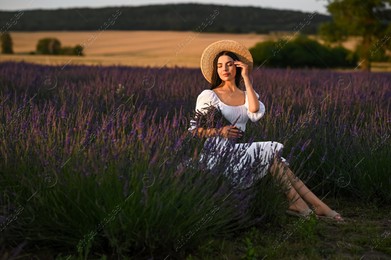 Beautiful young woman with bouquet sitting in lavender field at sunset Photo of Beautiful young woman with bouquet sitting in lavender field at sunset
