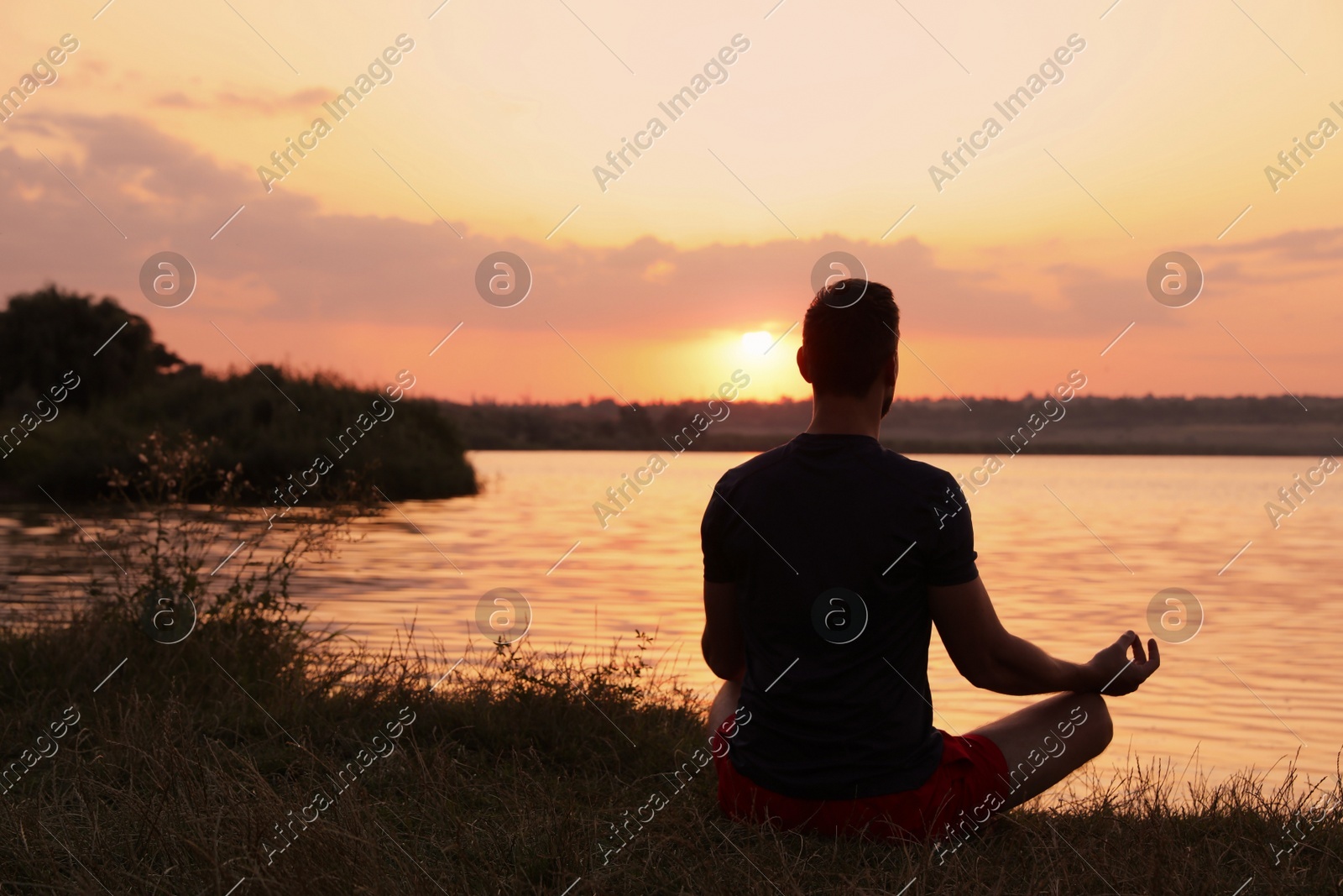 Man meditating near river at sunset, back view. Space for text Photo of Man meditating near river at sunset, back view. Space for text