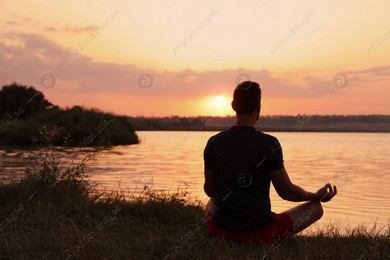 Man meditating near river at sunset, back view. Space for text Photo of Man meditating near river at sunset, back view. Space for text