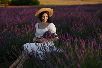 Beautiful young woman with bouquet sitting in lavender field at sunset Photo of Beautiful young woman with bouquet sitting in lavender field at sunset