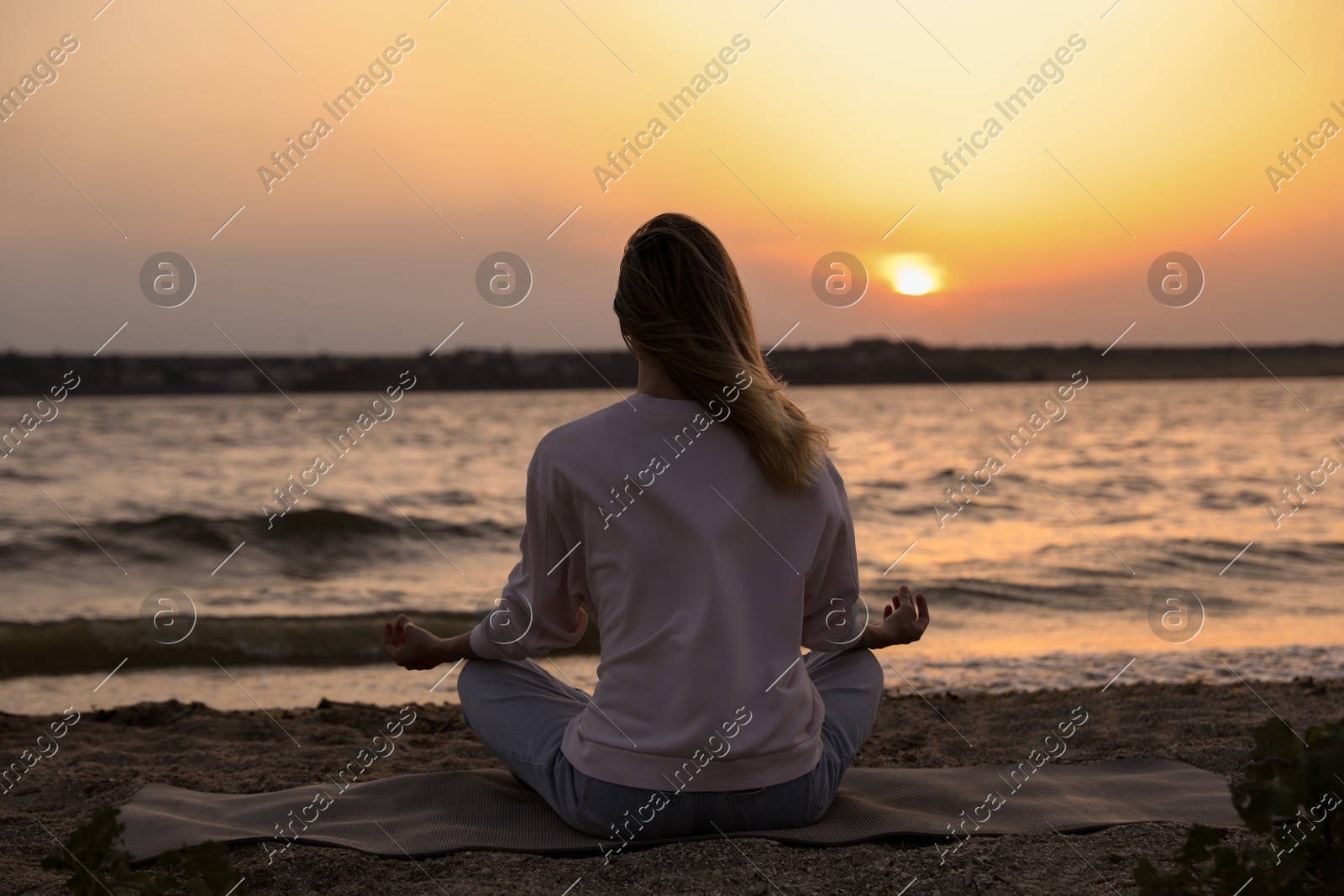 Young woman meditating on beach near river at sunset, back view Photo of Young woman meditating on beach near river at sunset, back view