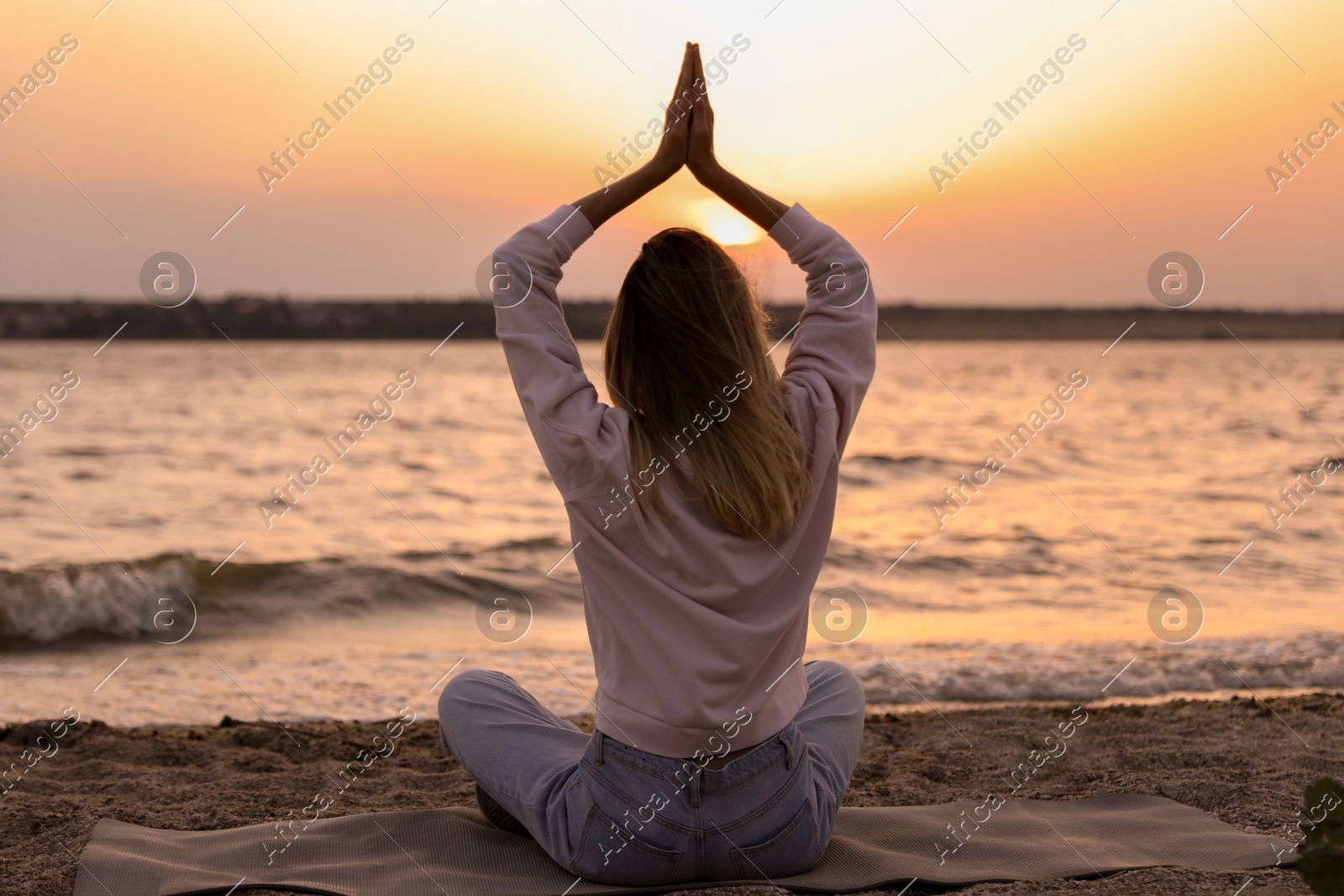 Young woman meditating on beach near river at sunset, back view Photo of Young woman meditating on beach near river at sunset, back view