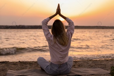 Young woman meditating on beach near river at sunset, back view Photo of Young woman meditating on beach near river at sunset, back view