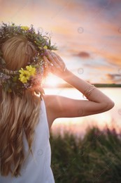 Young woman wearing wreath made of beautiful flowers outdoors at sunset Photo of Young woman wearing wreath made of beautiful flowers outdoors at sunset