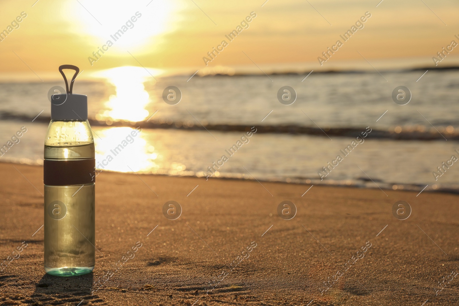 Glass bottle with water on wet sand near sea at sunset. Space for text Photo of Glass bottle with water on wet sand near sea at sunset. Space for text