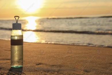 Glass bottle with water on wet sand near sea at sunset. Space for text Photo of Glass bottle with water on wet sand near sea at sunset. Space for text