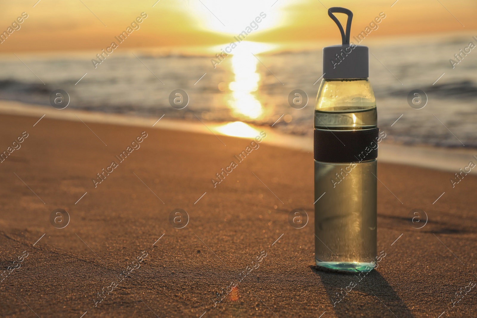 Glass bottle with water on wet sand near sea at sunset. Space for text Photo of Glass bottle with water on wet sand near sea at sunset. Space for text