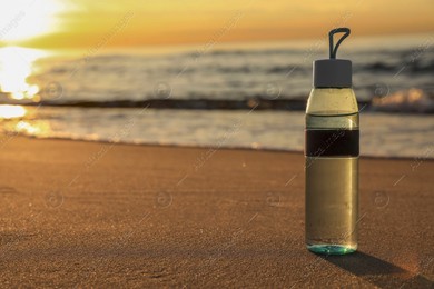 Glass bottle with water on wet sand near sea at sunset. Space for text Photo of Glass bottle with water on wet sand near sea at sunset. Space for text