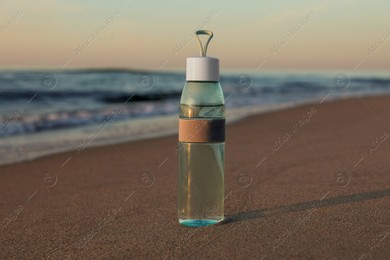 Glass bottle with water on wet sand near sea at sunset Photo of Glass bottle with water on wet sand near sea at sunset