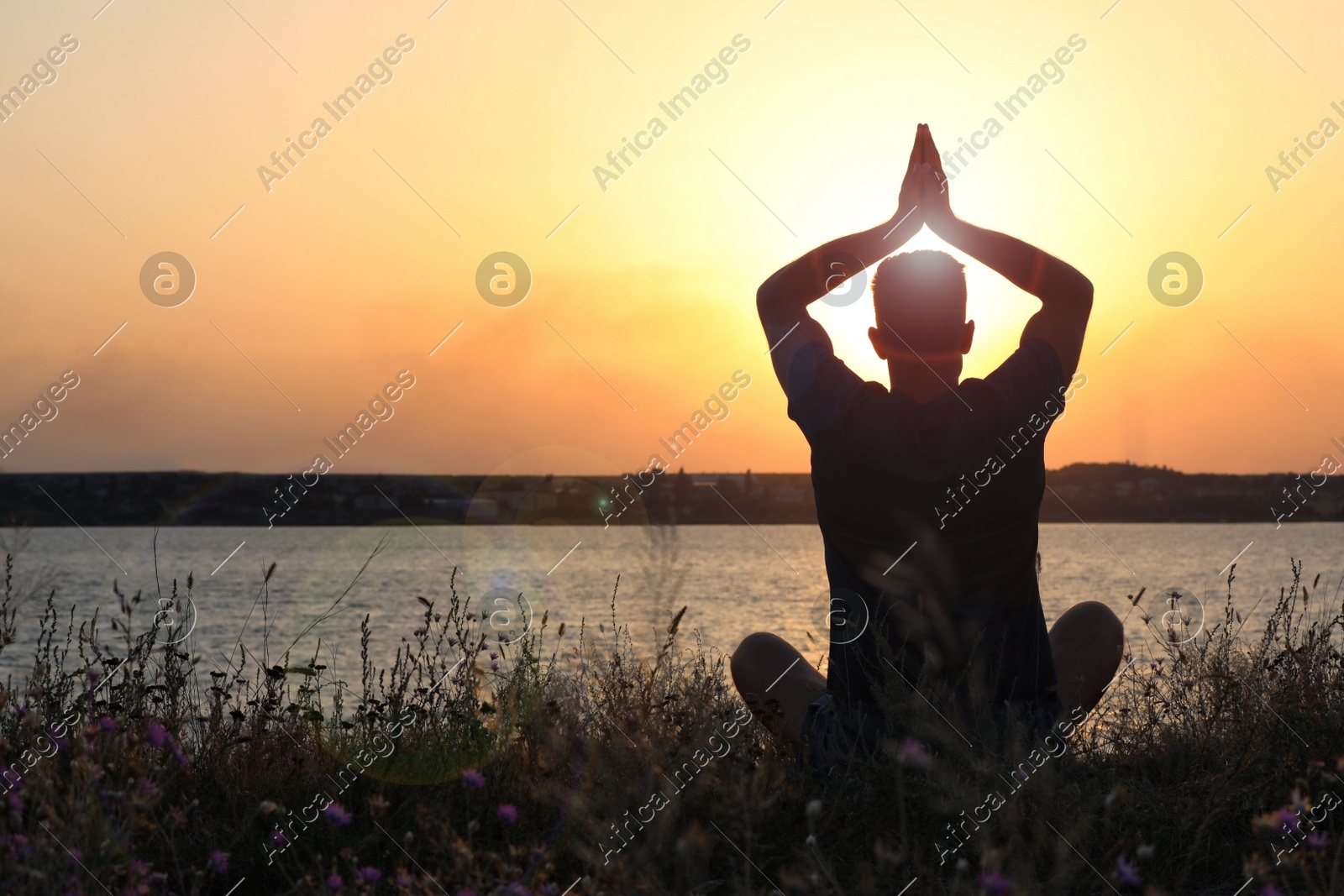 Man meditating near river at sunset, back view. Space for text Photo of Man meditating near river at sunset, back view. Space for text