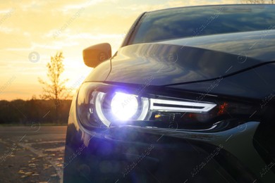 Black modern car parked on road at sunset, closeup of headlight Photo of Black modern car parked on road at sunset, closeup of headlight