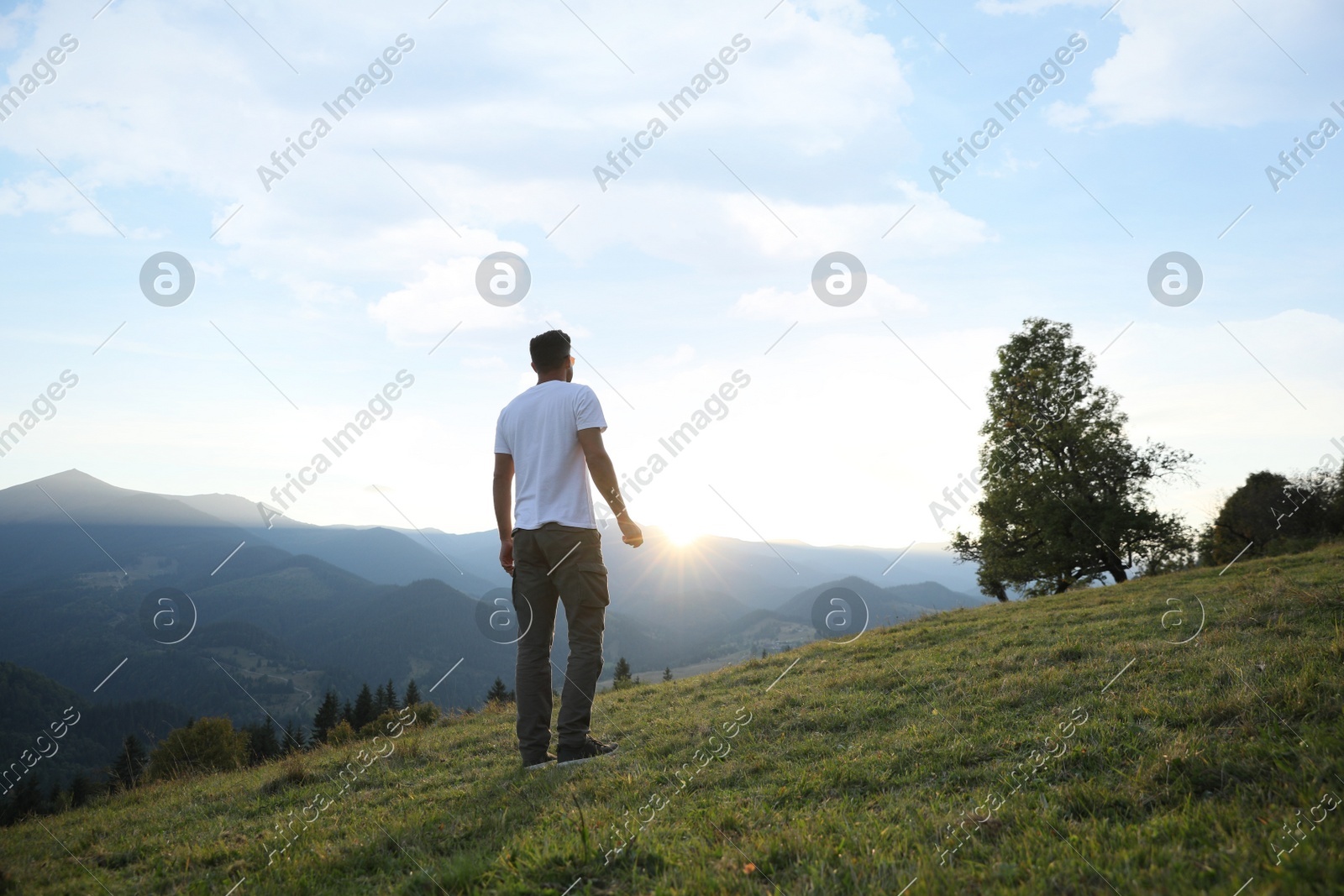 Man enjoying beautiful mountain landscape at sunset, back view Photo of Man enjoying beautiful mountain landscape at sunset, back view