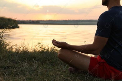 Man meditating near river at sunset, closeup. Space for text Photo of Man meditating near river at sunset, closeup. Space for text