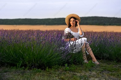 Beautiful young woman with bouquet sitting in lavender field at sunset Photo of Beautiful young woman with bouquet sitting in lavender field at sunset