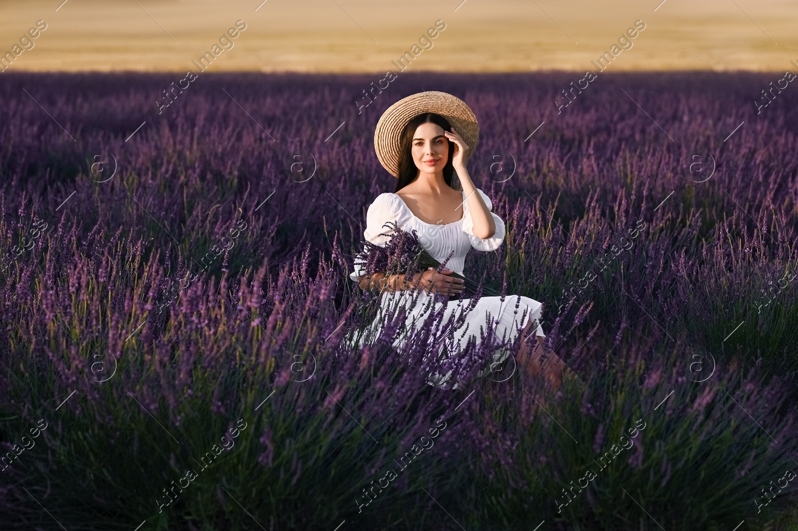 Beautiful young woman with bouquet sitting in lavender field at sunset Photo of Beautiful young woman with bouquet sitting in lavender field at sunset