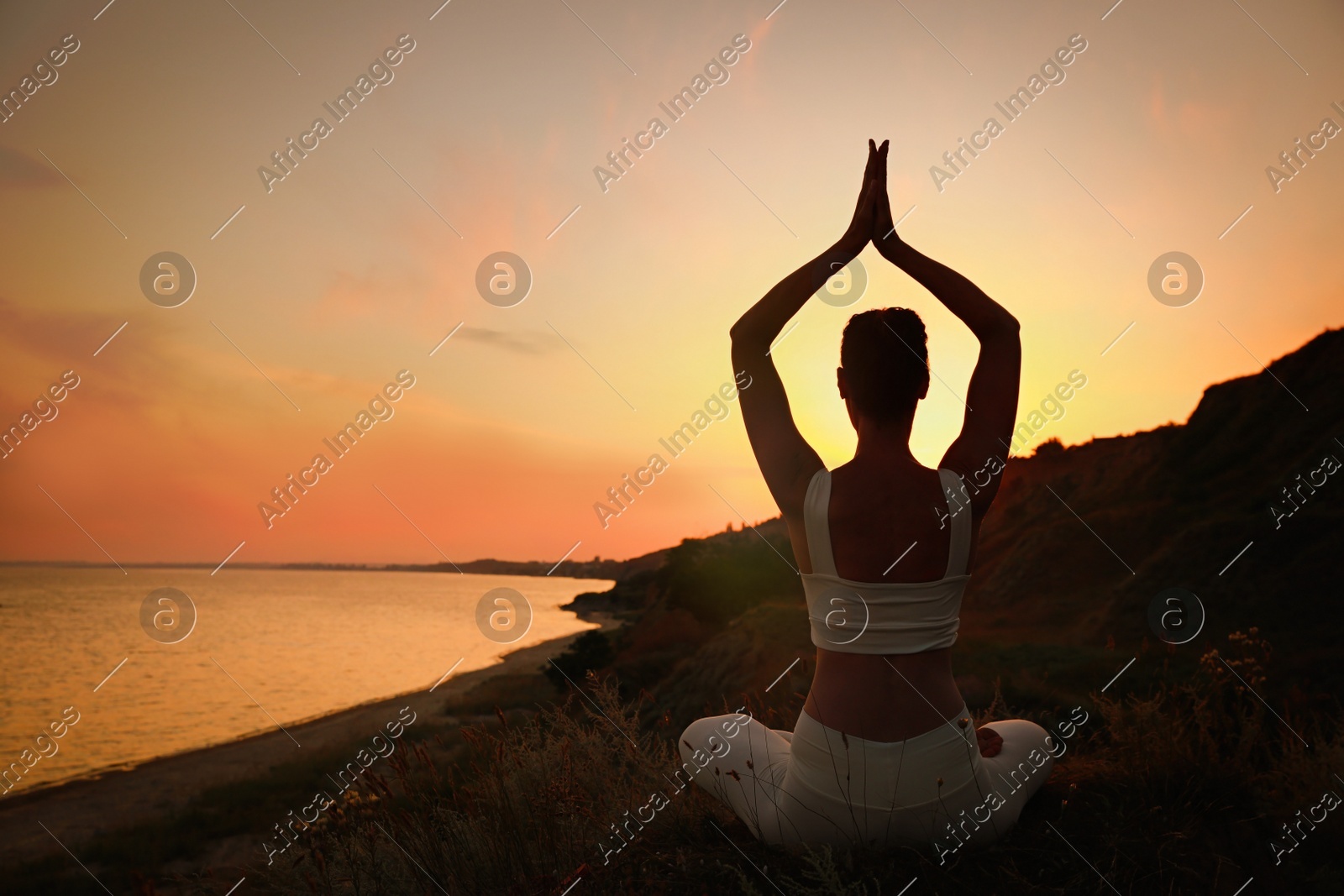 Woman meditating near sea at sunset, back view. Space for text Photo of Woman meditating near sea at sunset, back view. Space for text