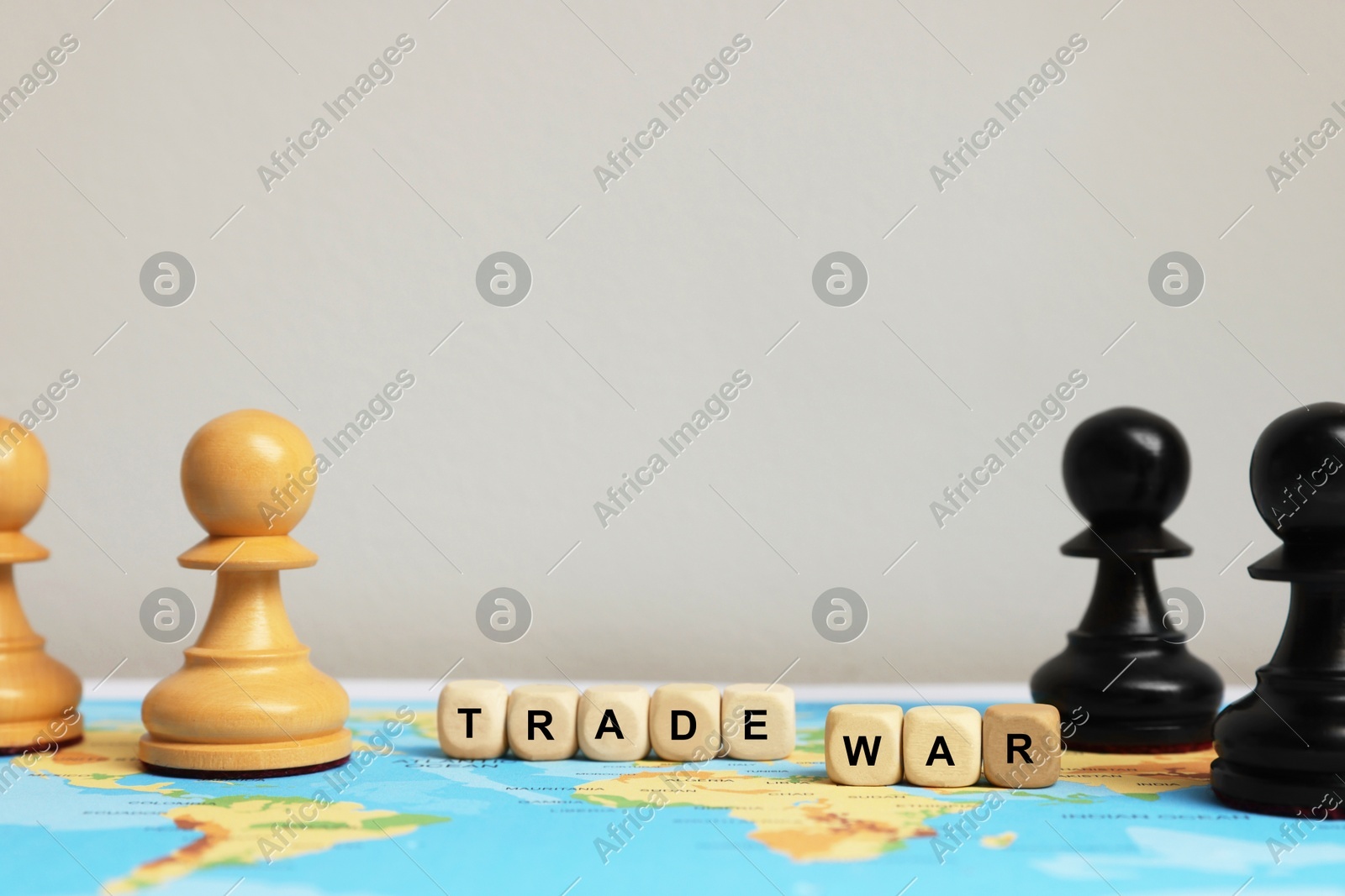 Wooden cubes with phrase Trade war and chess pieces on world map against light background Photo of Wooden cubes with phrase Trade war and chess pieces on world map against light background