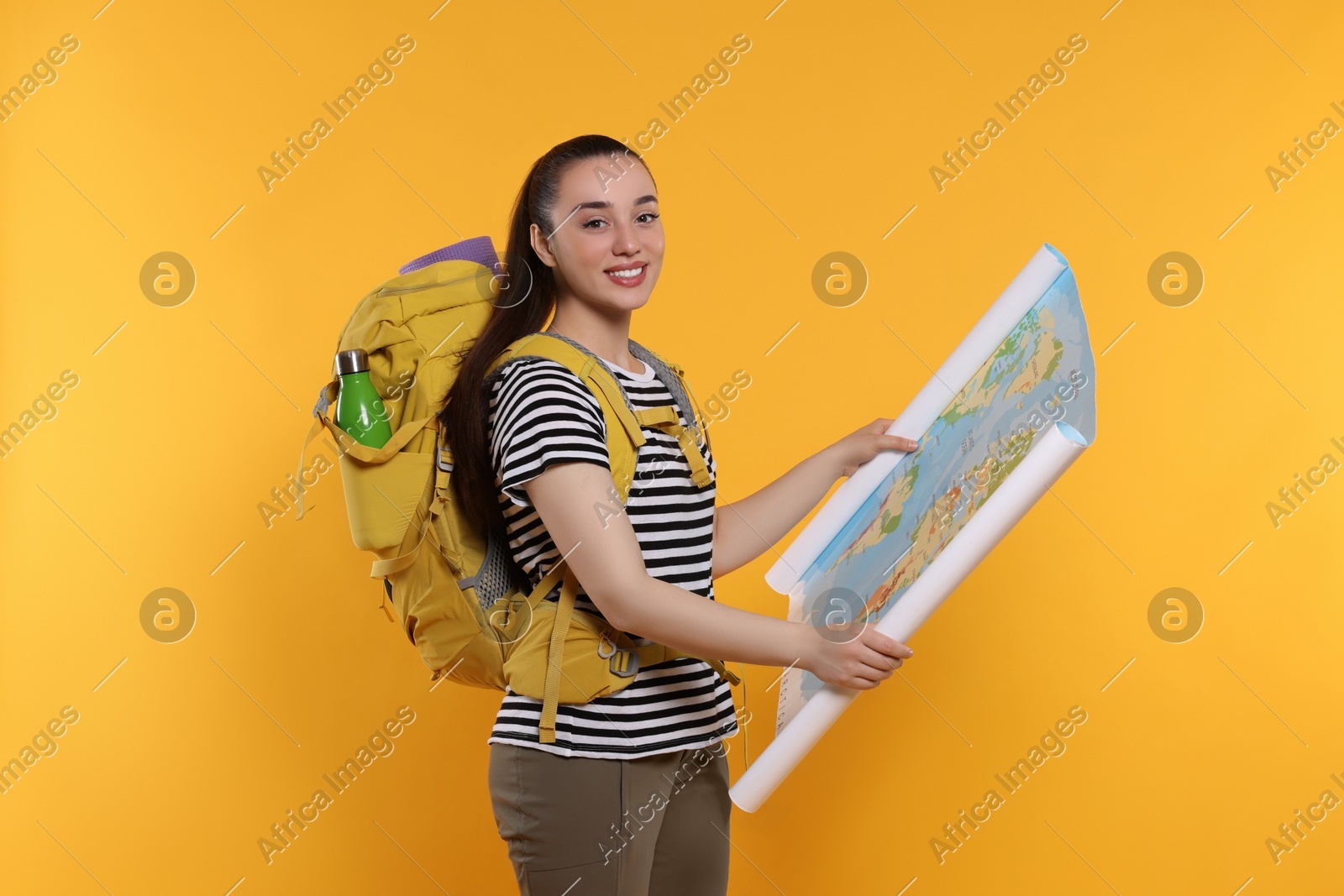Smiling young woman with backpack and map on orange background. Active tourism Photo of Smiling young woman with backpack and map on orange background. Active tourism