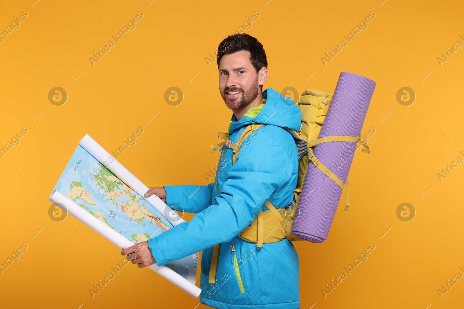 Happy man with backpack and map on orange background. Active tourism Photo of Happy man with backpack and map on orange background. Active tourism