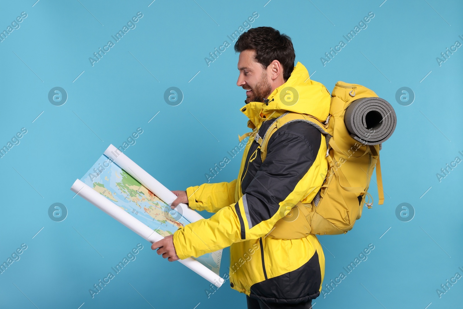 Happy man with backpack and map on light blue background. Active tourism Photo of Happy man with backpack and map on light blue background. Active tourism
