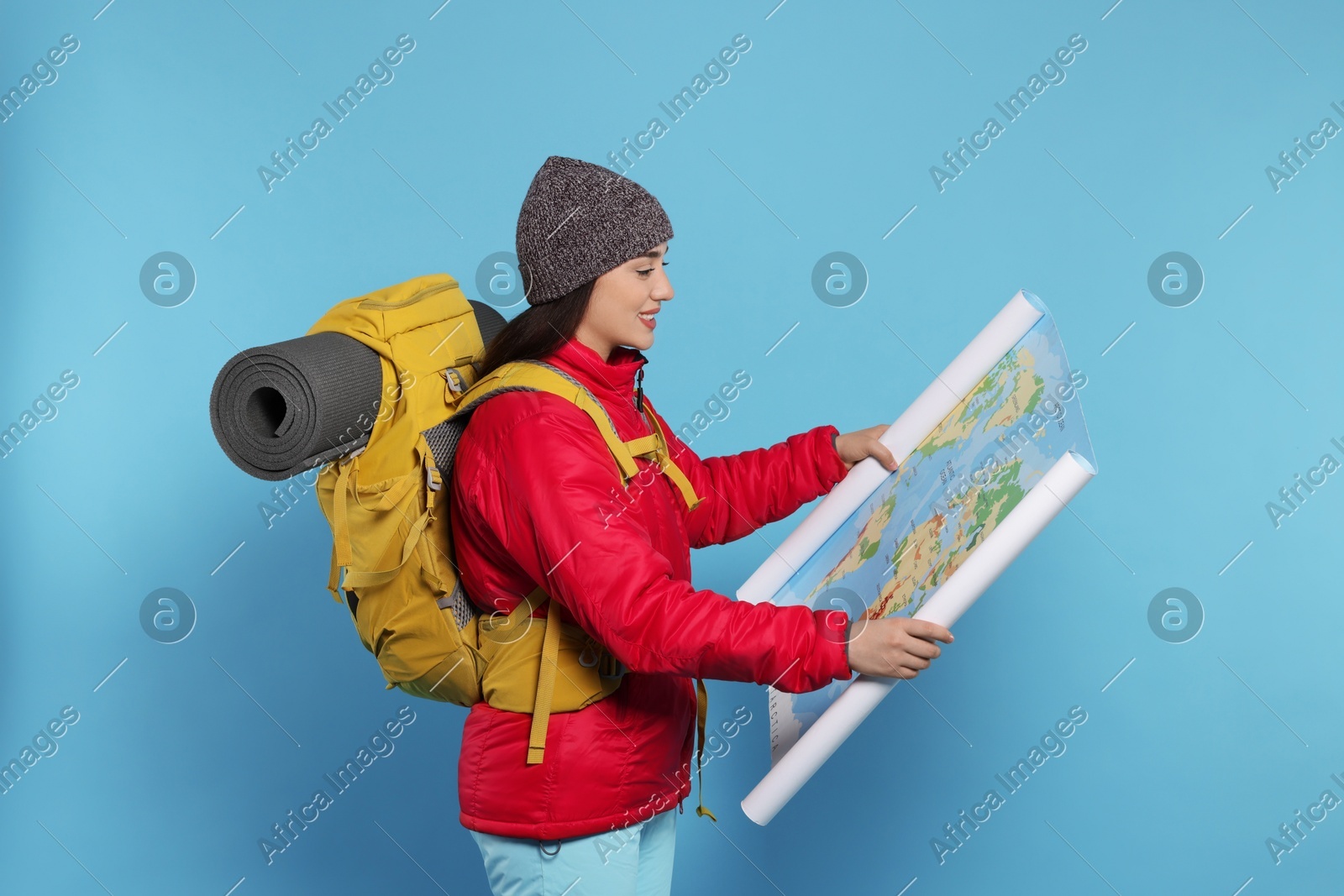 Smiling young woman with backpack and map on light blue background. Active tourism Photo of Smiling young woman with backpack and map on light blue background. Active tourism