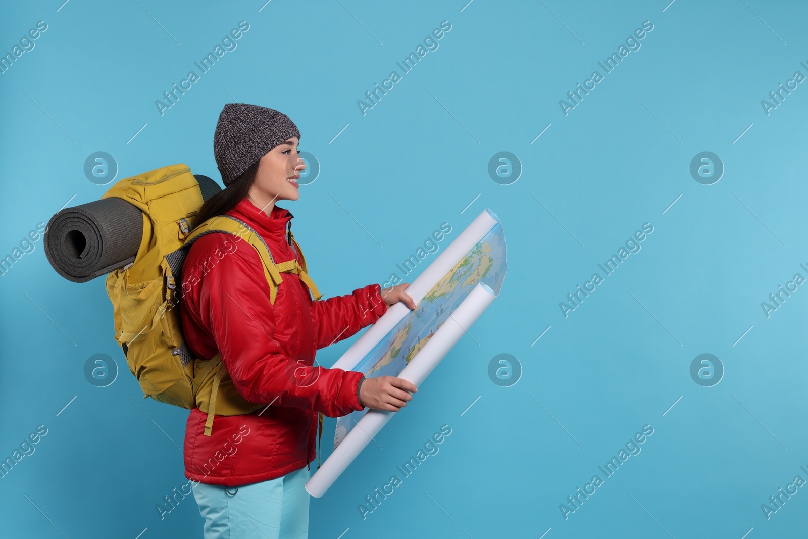 Smiling young woman with backpack and map on light blue background, space for text. Active tourism Photo of Smiling young woman with backpack and map on light blue background, space for text. Active tourism