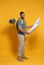 Happy tourist with backpack and map on yellow background Photo of Happy tourist with backpack and map on yellow background