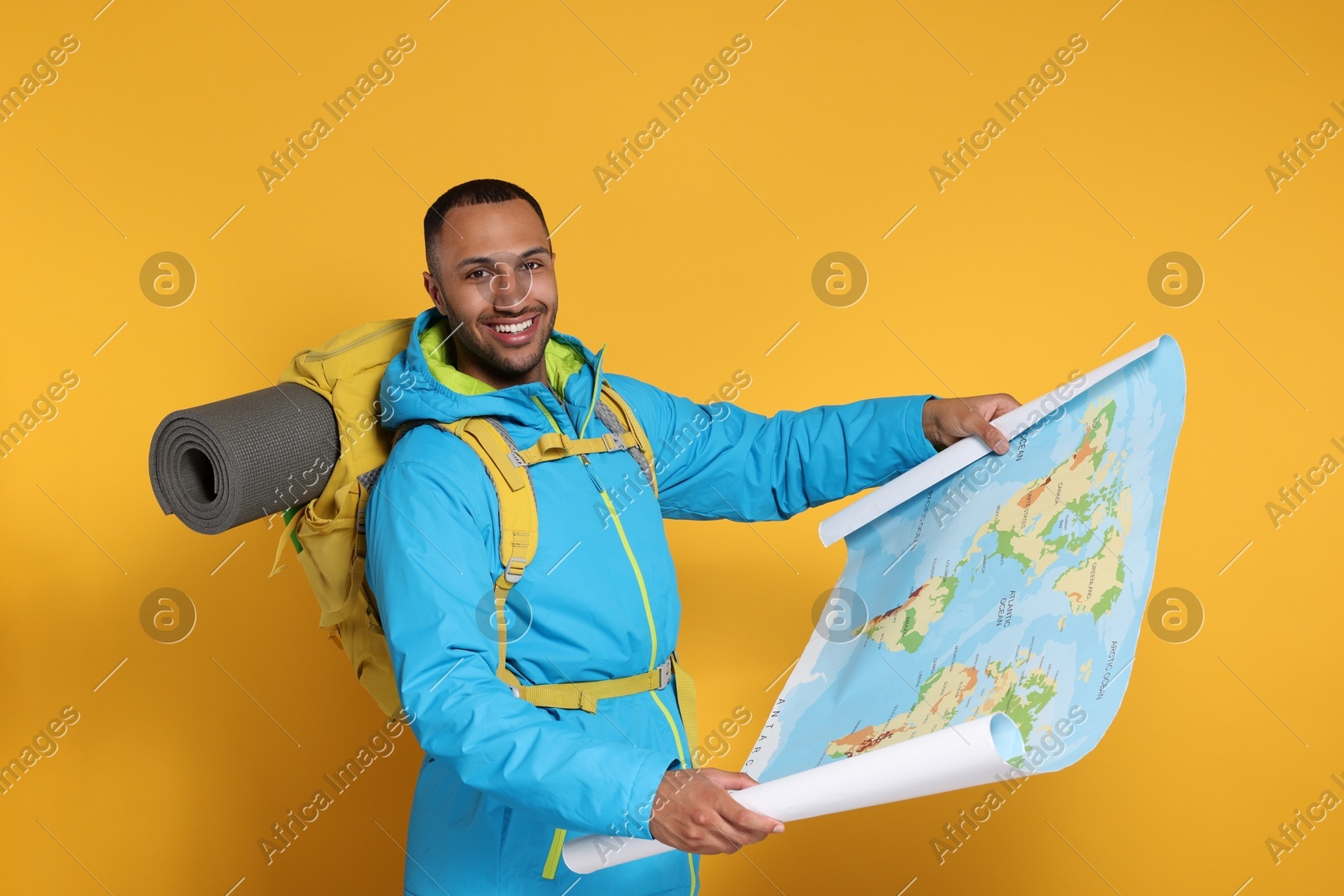 Happy tourist with backpack and map on yellow background Photo of Happy tourist with backpack and map on yellow background