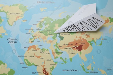 Paper airplane with word Propaganda on world map, top view. Information warfare concept Photo of Paper airplane with word Propaganda on world map, top view. Information warfare concept