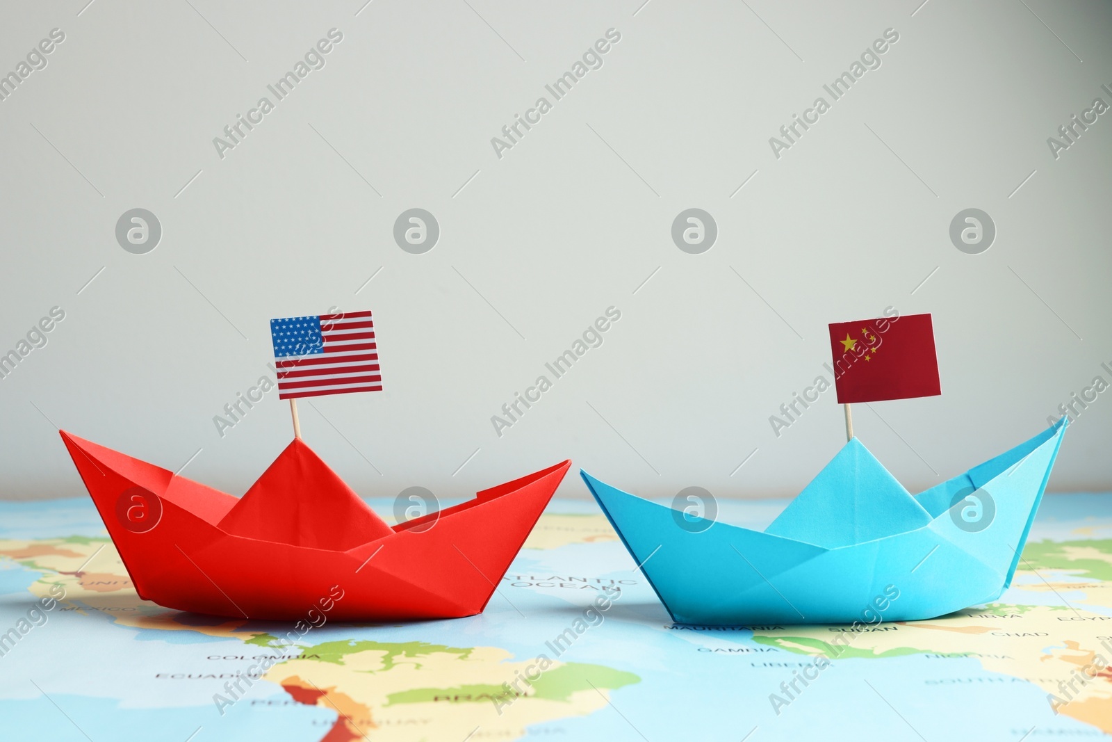 Paper boats with USA and China flags on world map against light background. Trade war concept Photo of Paper boats with USA and China flags on world map against light background. Trade war concept