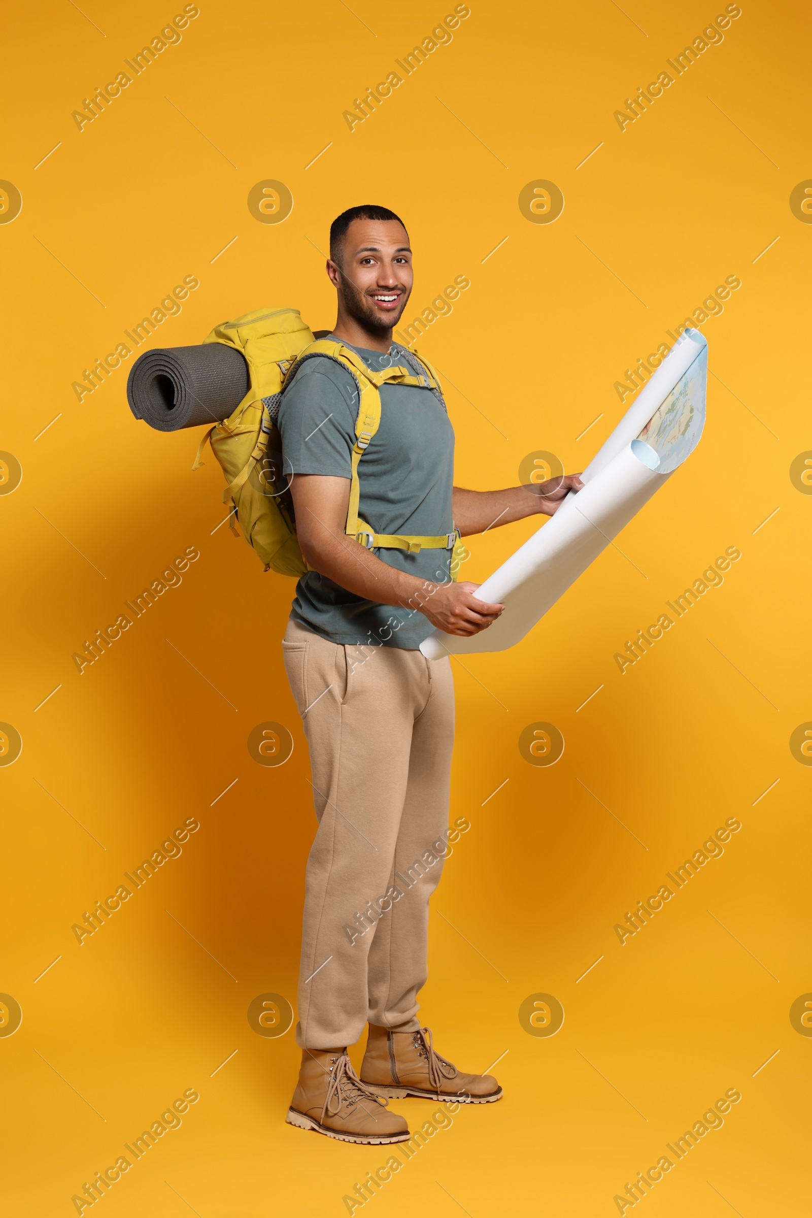 Happy tourist with backpack and map on yellow background Photo of Happy tourist with backpack and map on yellow background