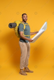 Happy tourist with backpack and map on yellow background Photo of Happy tourist with backpack and map on yellow background