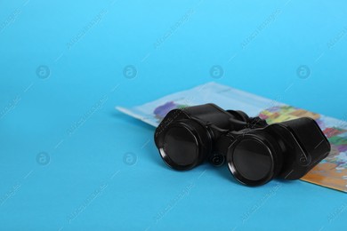 Modern binoculars and map on light blue background, space for text Photo of Modern binoculars and map on light blue background, space for text