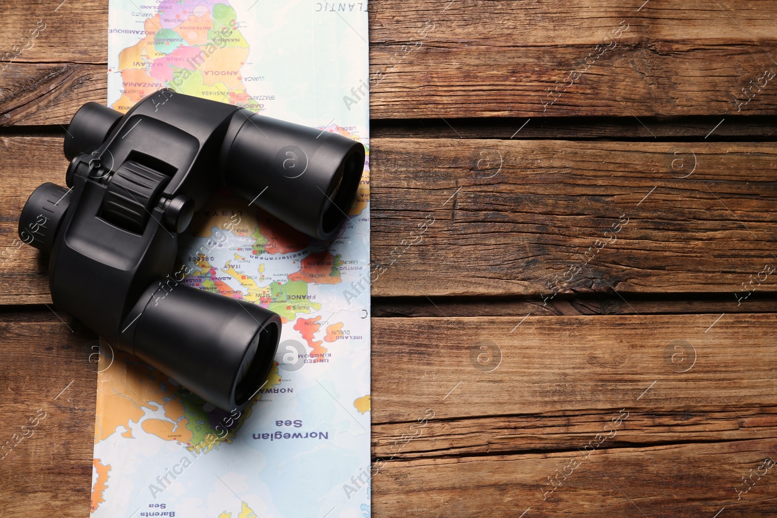 Modern binoculars and map on wooden table, top view. Space for text Photo of Modern binoculars and map on wooden table, top view. Space for text